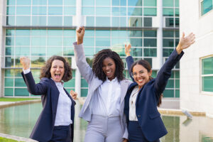 Three smiling businesswomen making winner gestures and rejoicing at corporate success