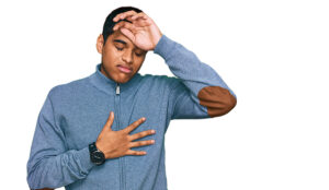 Young man wearing casual sweatshirt touching forehead for illness and fever