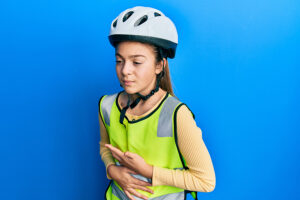 Young girl wearing a bike helmet feeling unwell with her hand on her stomach