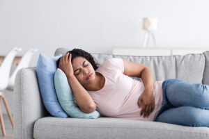 Sick woman lying on sofa holding her painful stomach