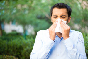 Young man with allergies blowing his nose outside