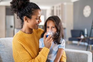 Mother helping her daughter use a nebulizer for common cold treatment