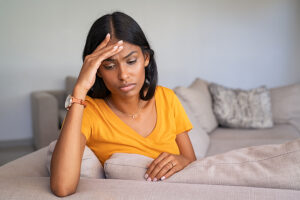 Woman sitting on a couch at home dealing with a headache