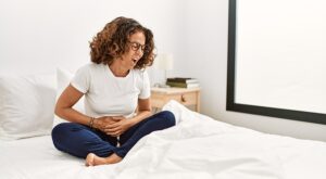 Woman sitting cross-legged on her bed feeling nauseous and holding her stomach