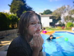 Young girl standing by swimming pool with her face covered in sunscreen