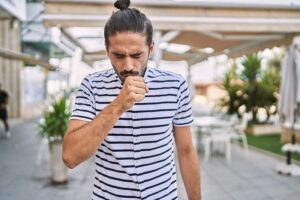 Young man walking through city courtyard feeling unwell and coughing