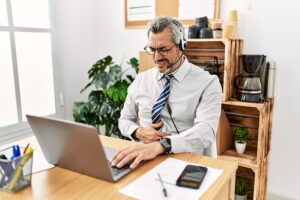 Businessman working at office wearing headset with hand on stomach due to indigestion