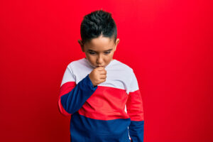 Little boy wearing red, white, and blue sweater feeling unwell and coughing