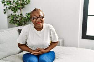 Woman sitting on edge of bed feeling nauseous and holding her stomach