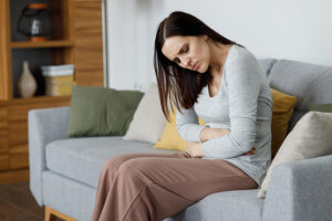 Young woman with painful UTI sitting on couch at home