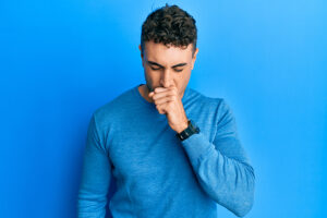 Young man in blue shirt coughing