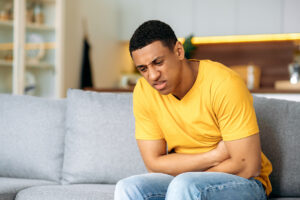 Young man with stomach pain sitting on couch at home