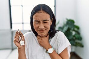 Young woman grimacing and touching her painful sore throat