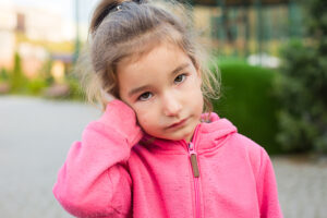 Little girl in pink jacket holding her painful ear