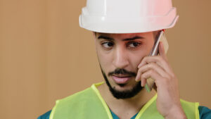 Male construction engineer wearing hard hat and talking on mobile phone about occupational health services