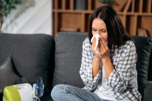 Young woman sick at home sitting on sofa and blowing her nose